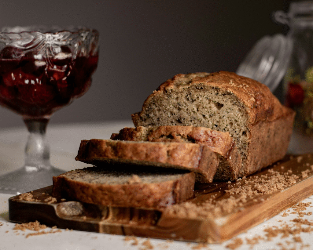 Freshly baked banana bread loaf on a wooden cutting board with sliced bananas on the side.