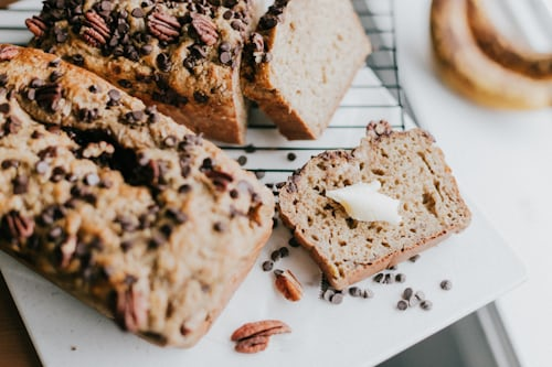 Golden brown homemade banana bread sliced on a white plate with a cup of coffee.