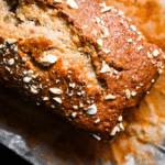 Sliced moist banana bread on a wooden board with fresh bananas in the background.