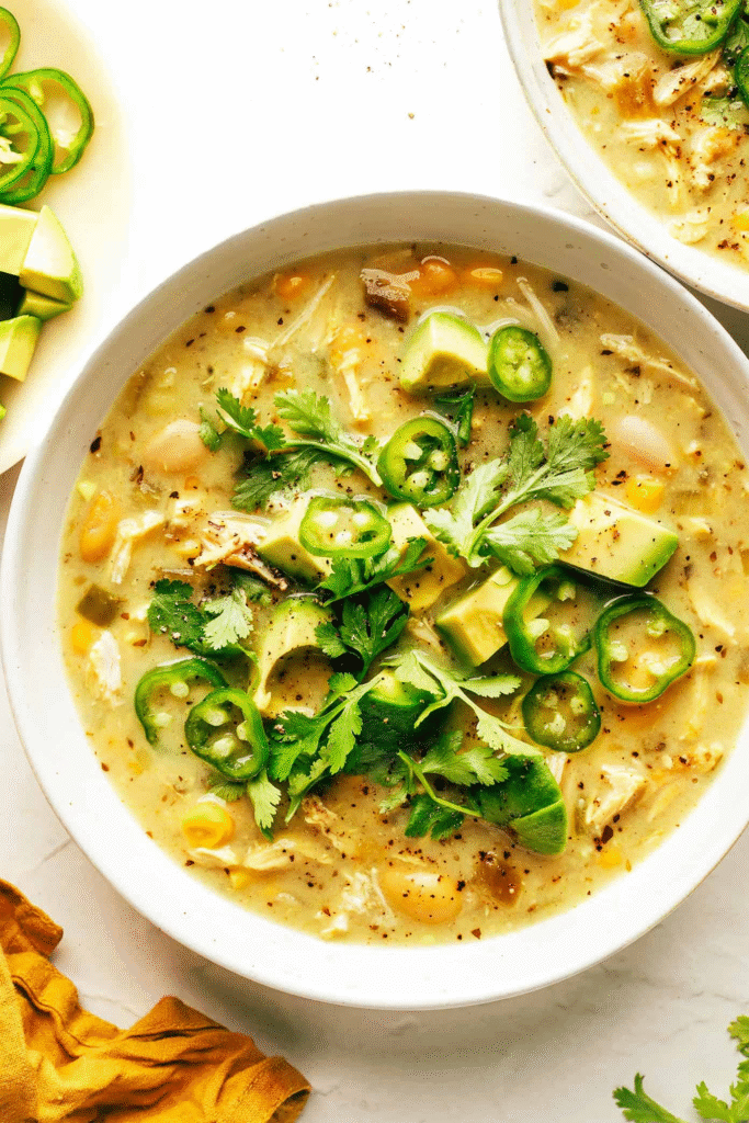 A close-up of a bowl of creamy white chicken chili with melted cheese and a garnish of cilantro.